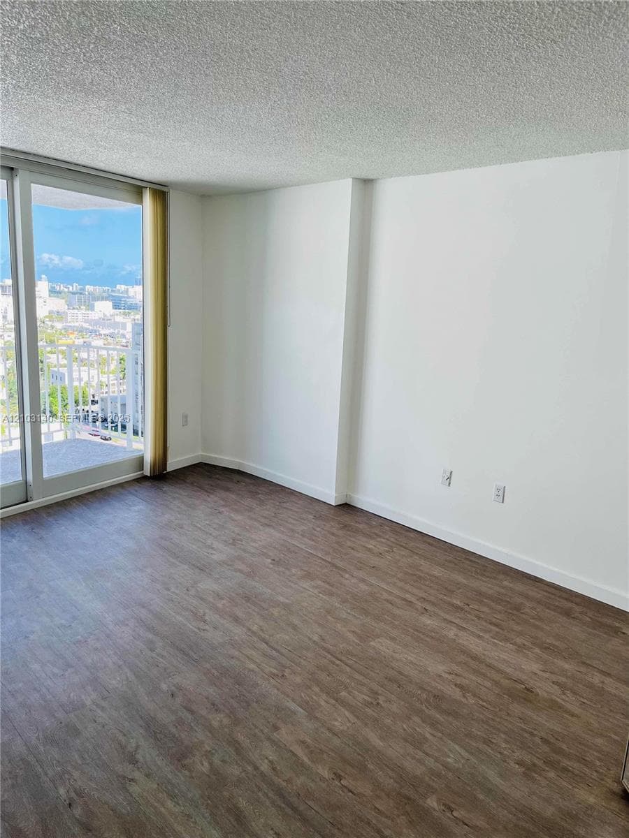 Room featuring wood-finish flooring, textured ceiling, and floor-to-ceiling glass sliding doors opening to an exterior balcony