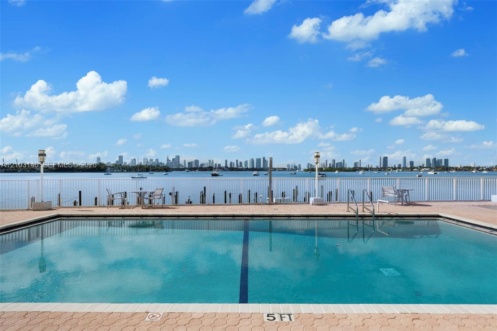 Rectangular swimming pool with paved decking, metal perimeter fencing, and water backdrop