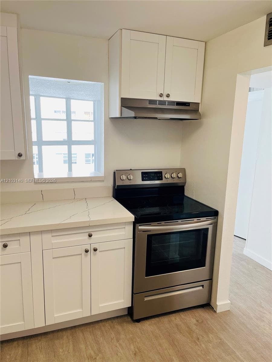 Kitchen area featuring white shaker-style cabinetry, white countertops with integrated backsplash, stainless steel electric range, stainless steel range hood, and wood-finish flooring