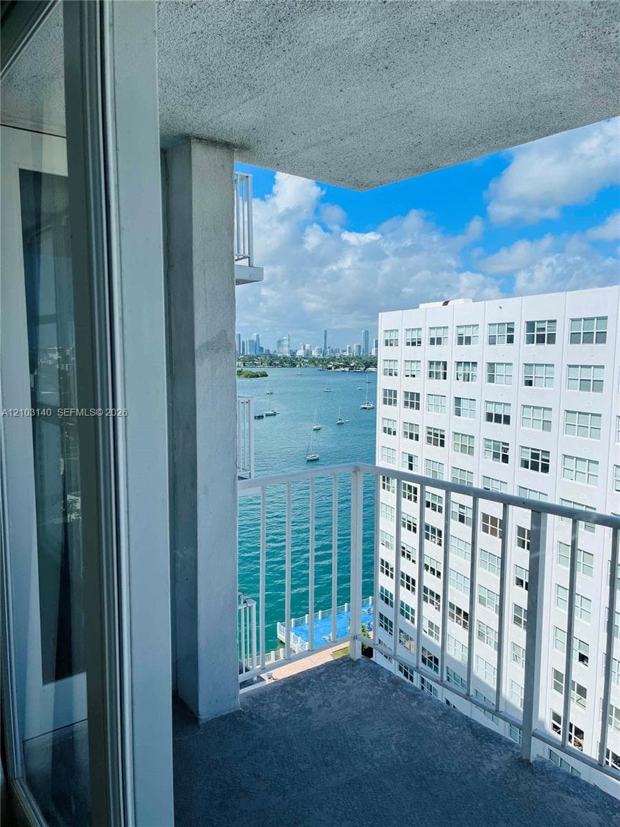Private balcony with a metal railing and concrete flooring, featuring an expansive water and urban skyline backdrop