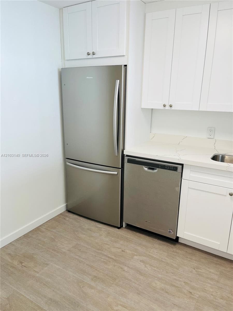 Kitchen featuring white shaker-style cabinetry, stainless steel refrigerator and dishwasher, stone-finish countertops, and wood-finish flooring