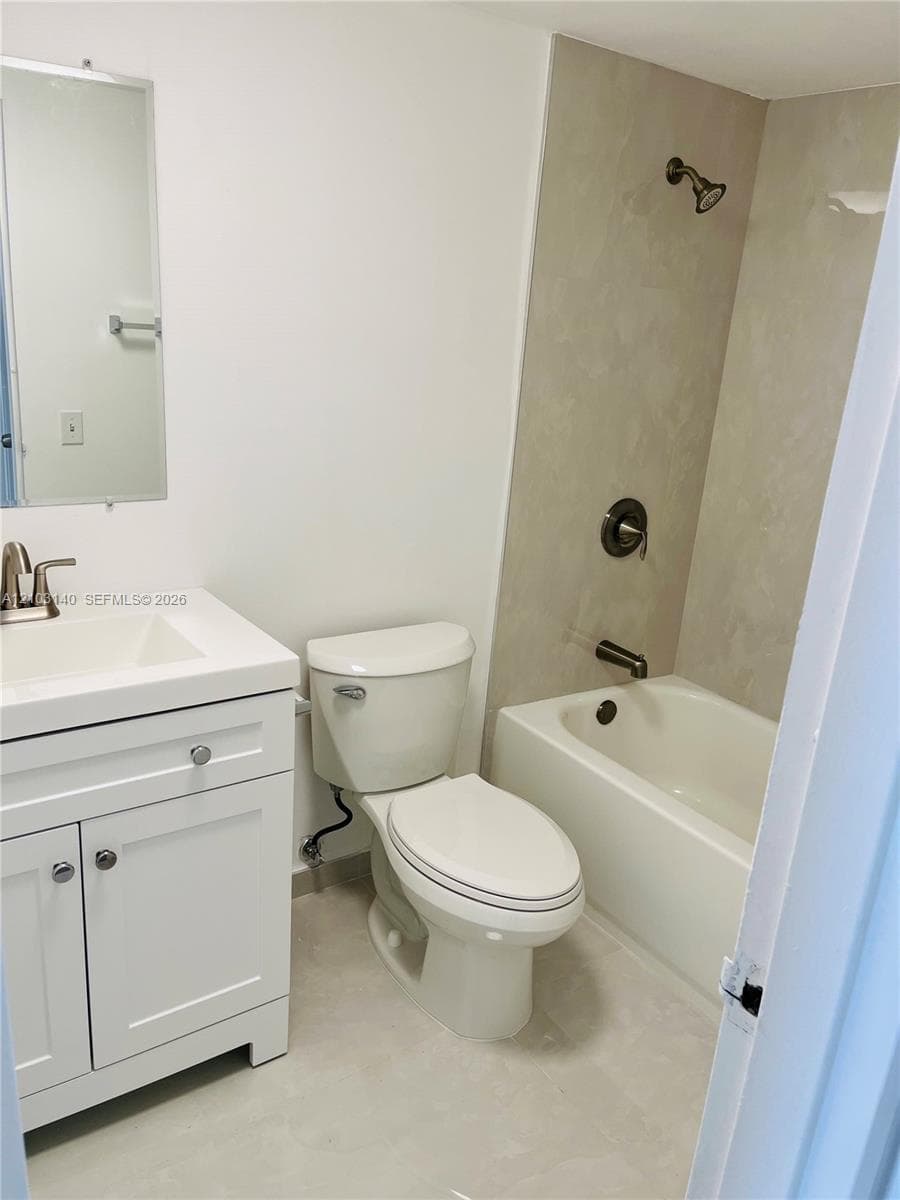 White vanity with a rectangular sink, wall-mounted mirror, two-piece toilet, and tub-shower combination featuring neutral wall surround and metallic fixtures