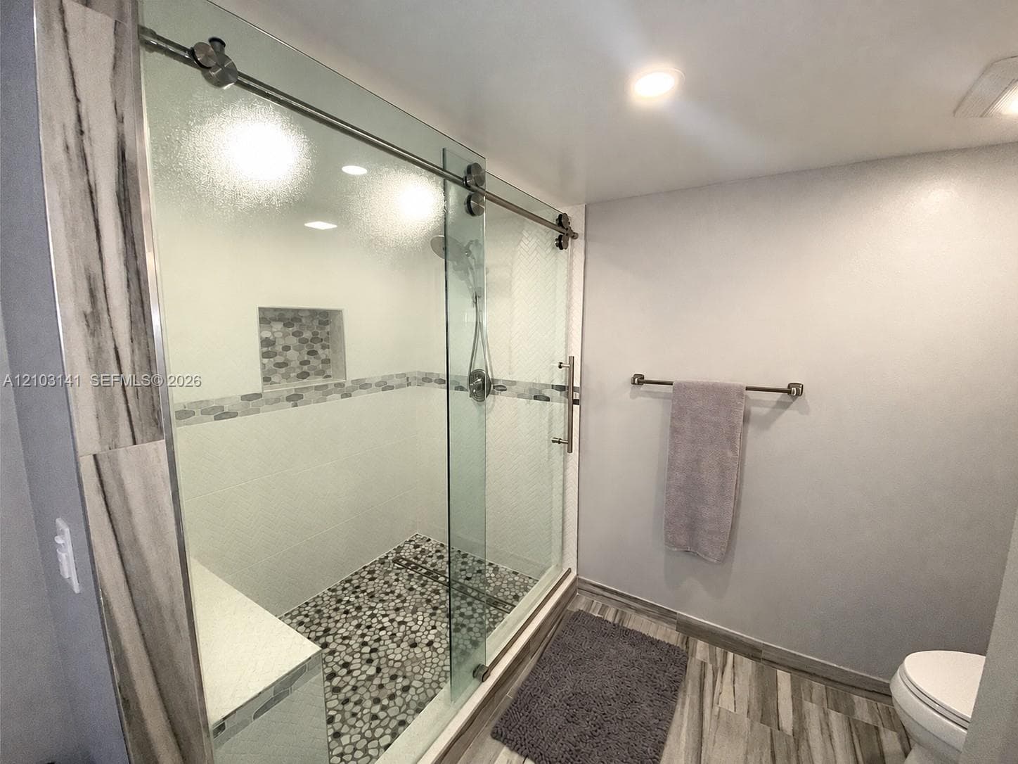 Walk-in shower featuring a sliding glass enclosure, pebble-stone flooring, an integrated tiled recessed niche, and a brushed nickel rainfall shower head