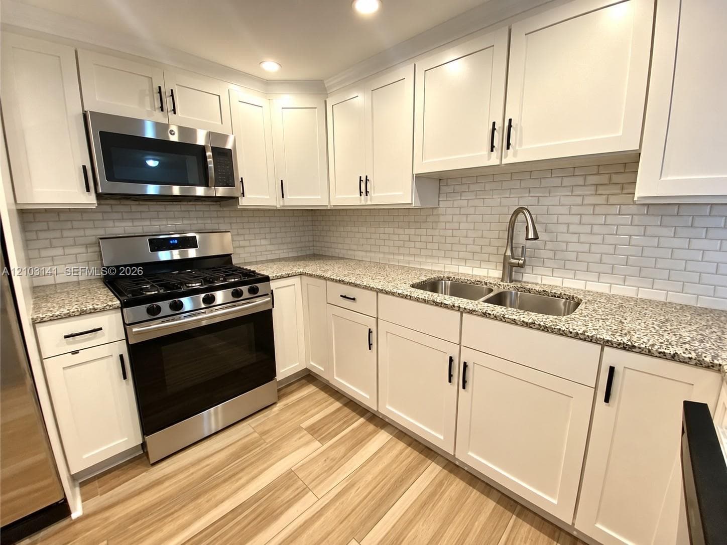 Kitchen featuring white shaker-style cabinetry, speckled stone countertops, a subway tile backsplash, stainless steel gas range with built-in microwave, and wood-finish flooring