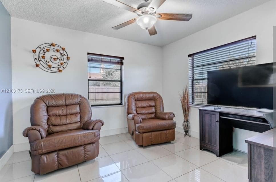 Neutral-toned tile flooring, dual windows with horizontal blinds, and a central ceiling fan with integrated lighting