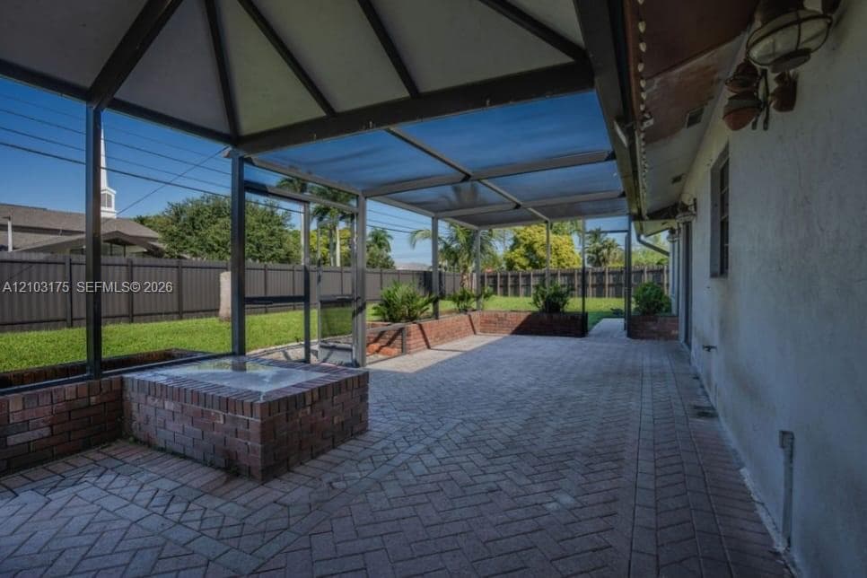 Screened-in patio featuring herringbone brick pavers, a built-in brick planter, and a vaulted metal frame enclosure