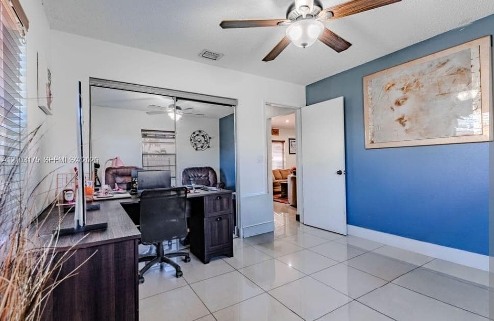Neutral tile flooring, ceiling fan with light fixture, mirrored closet doors, and a bold accent wall
