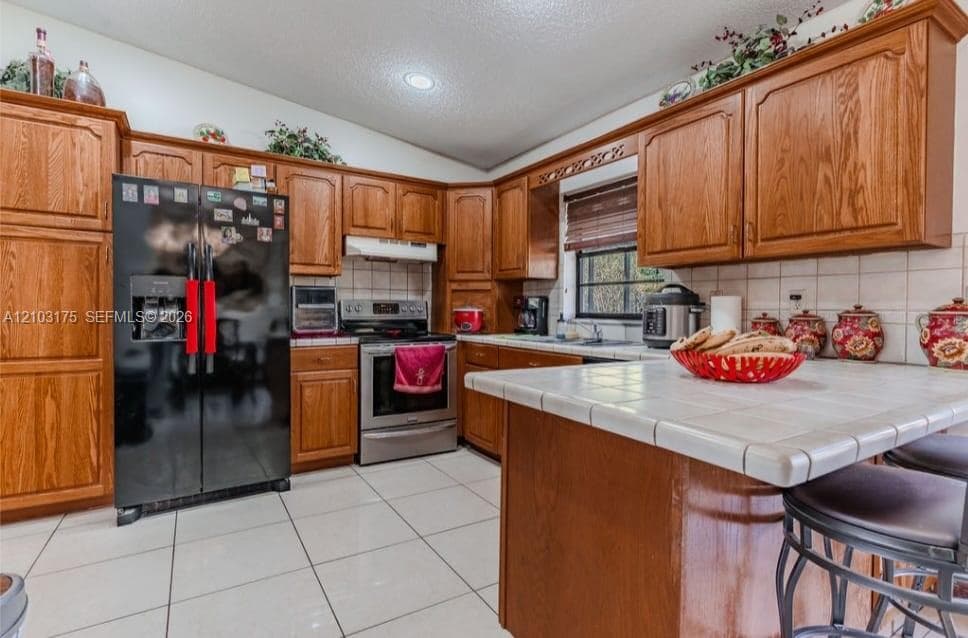 Kitchen featuring wood cabinetry, tile countertops, tile flooring, recessed lighting, and stainless steel appliances