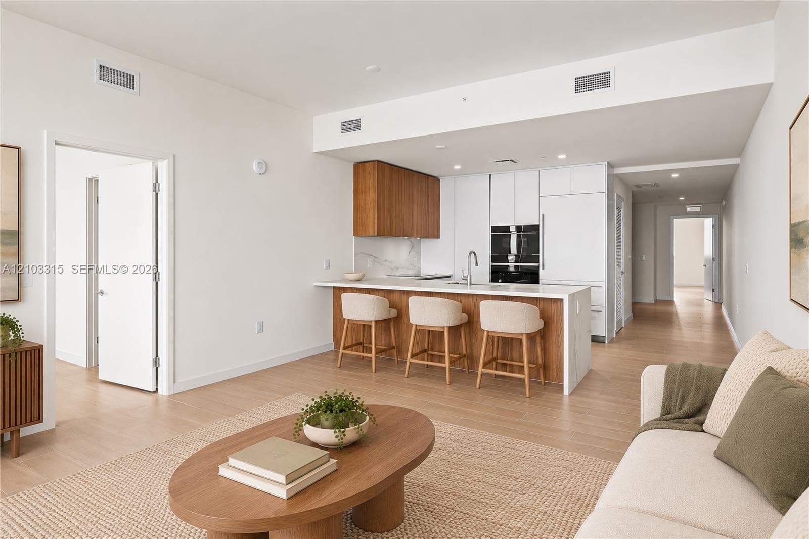 Open-concept living space featuring wood-finish flooring, a kitchen island with seating, integrated appliances, and recessed lighting