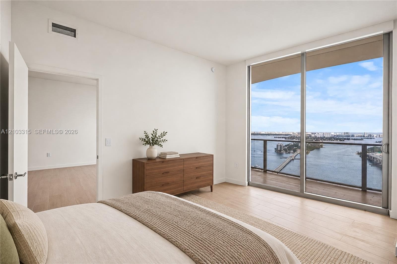Floor-to-ceiling sliding glass doors, water scenery, light wood-finish flooring, white walls, and an additional bright room