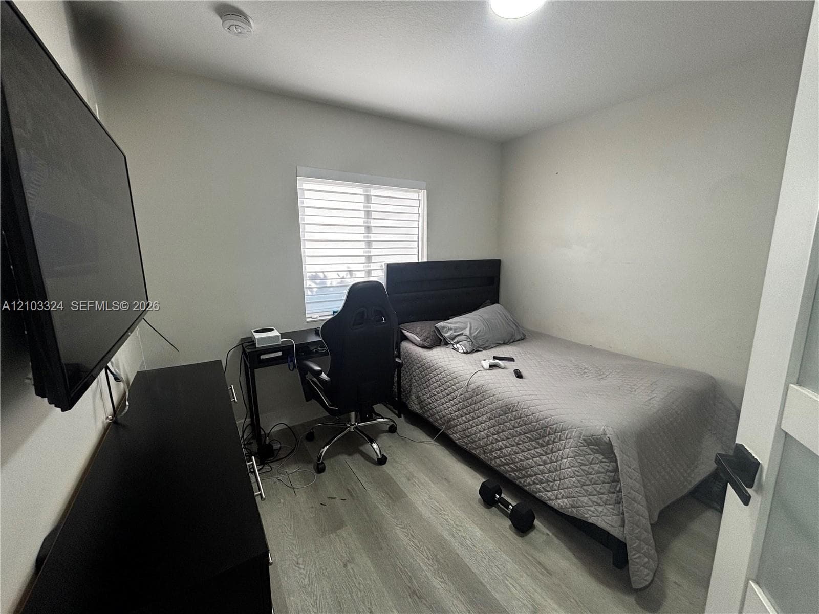Bedroom featuring wood-finish flooring, a neutral color palette, and a window with horizontal blinds