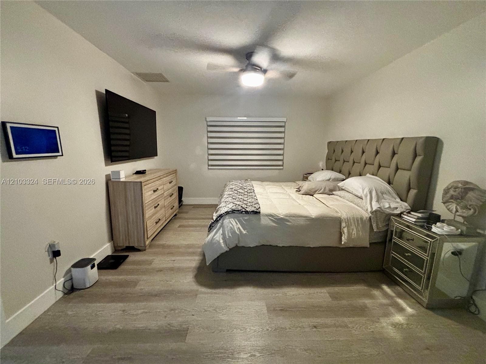 Neutral-toned interior featuring wood-finish flooring, a ceiling fan with integrated lighting, and horizontal window blinds