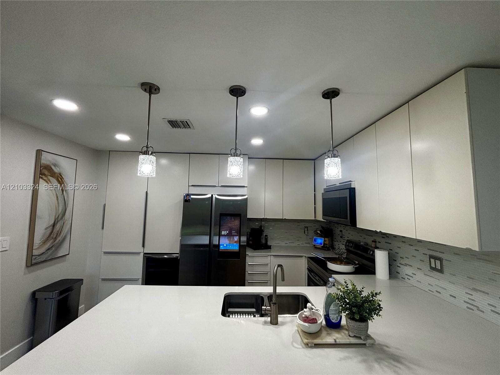 Kitchen featuring slab countertops, flat-panel cabinetry, recessed lighting, glass pendant fixtures, and a dual-basin undermount sink with a gooseneck faucet
