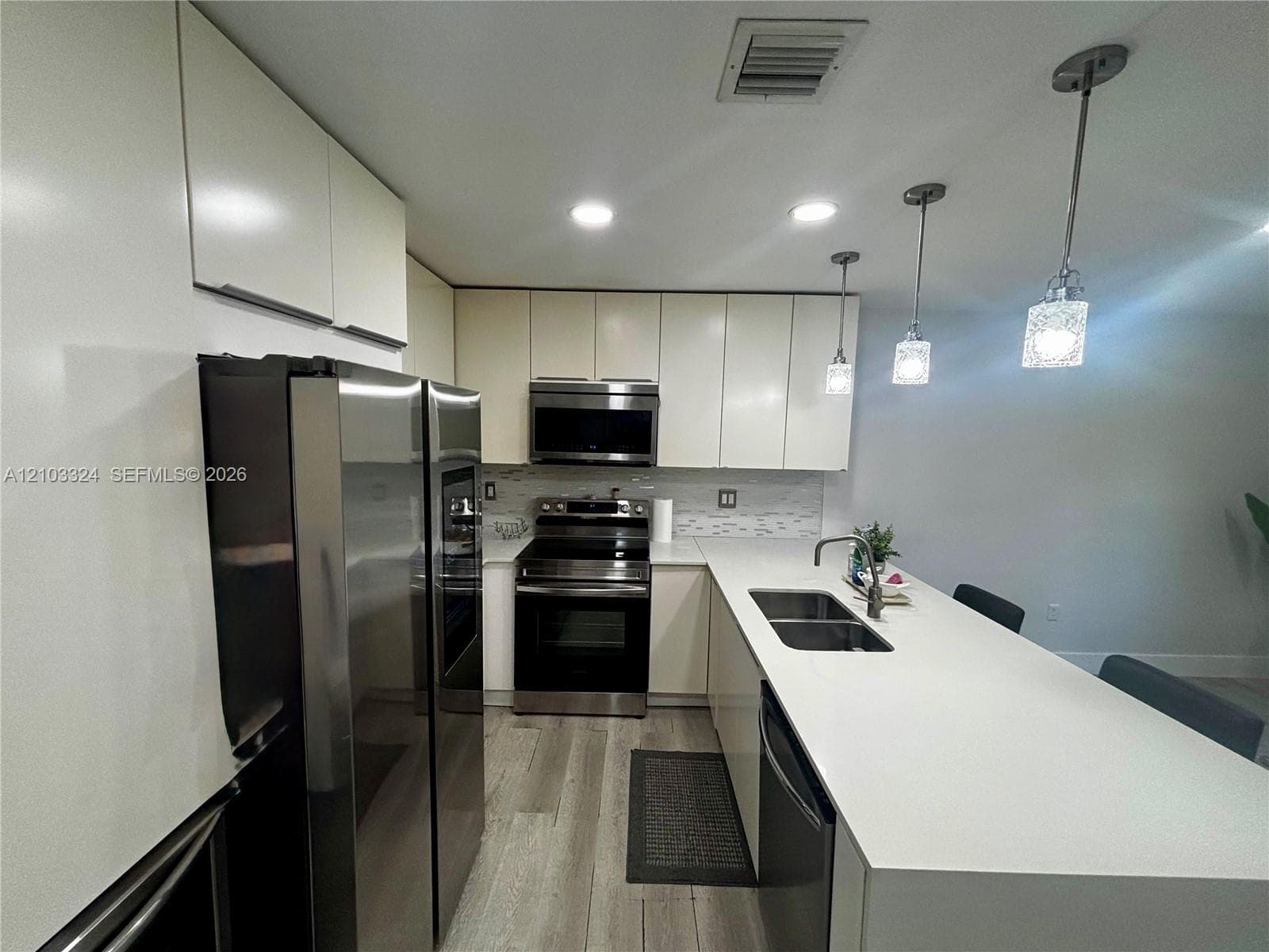 Kitchen featuring flat-panel cabinetry, quartz countertops, a double-basin stainless steel sink with a pull-down faucet, stainless steel appliances, and wood-finish flooring
