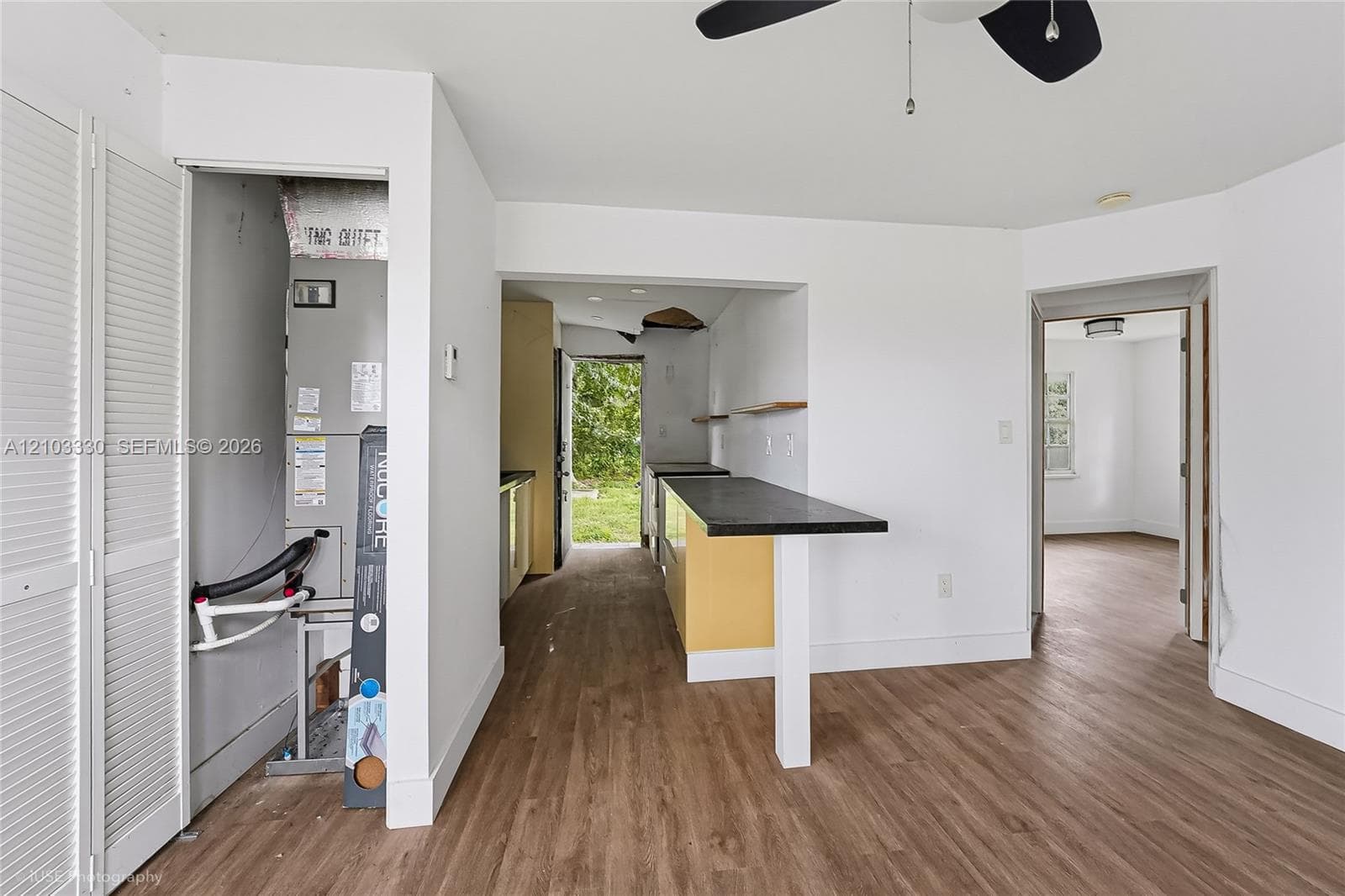 Interior space featuring wood-finish flooring, a built-in counter surface with a dark countertop, white louvered closet doors, and a ceiling-mounted fan