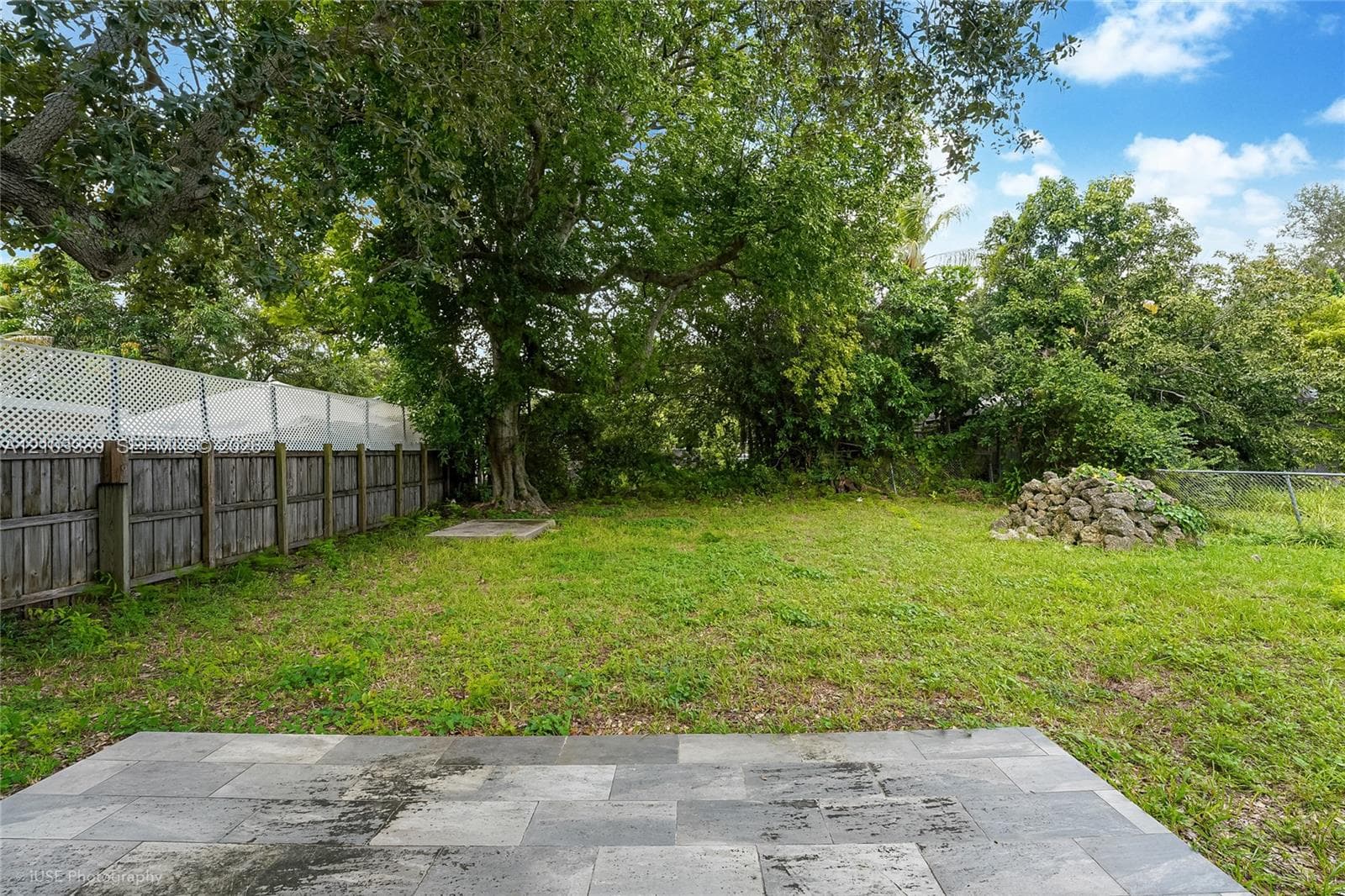 Backyard featuring a rectangular stone paver patio, wood privacy fencing with integrated lattice topper, and mature canopy trees