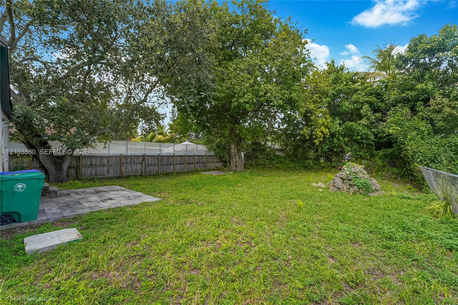 Backyard featuring a paved patio area, mature trees, wood privacy fencing, and a stone garden feature