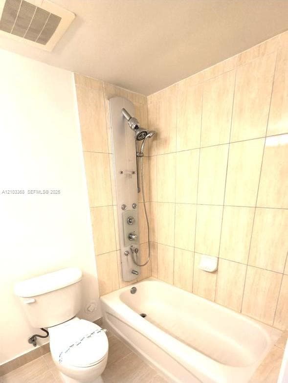 Bathtub featuring a wall-mounted shower panel system with multiple spray settings, hand-held sprayer, and floor-to-ceiling neutral ceramic wall tiling