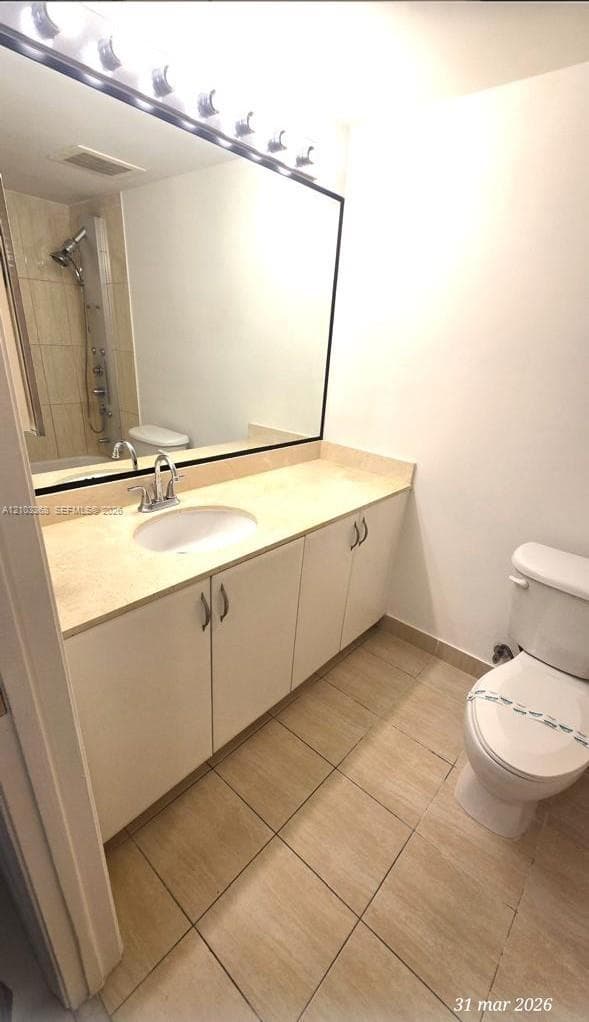 Bathroom featuring a vanity with integrated sink and stone-finish countertop, full-width mirror, multi-bulb lighting fixture, and tile flooring