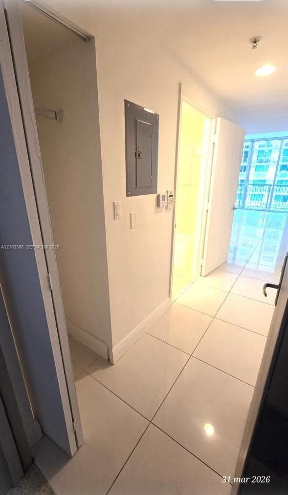 Hallway featuring large-format ceramic floor tiles, recessed ceiling lighting, and a floor-to-ceiling glass panel door