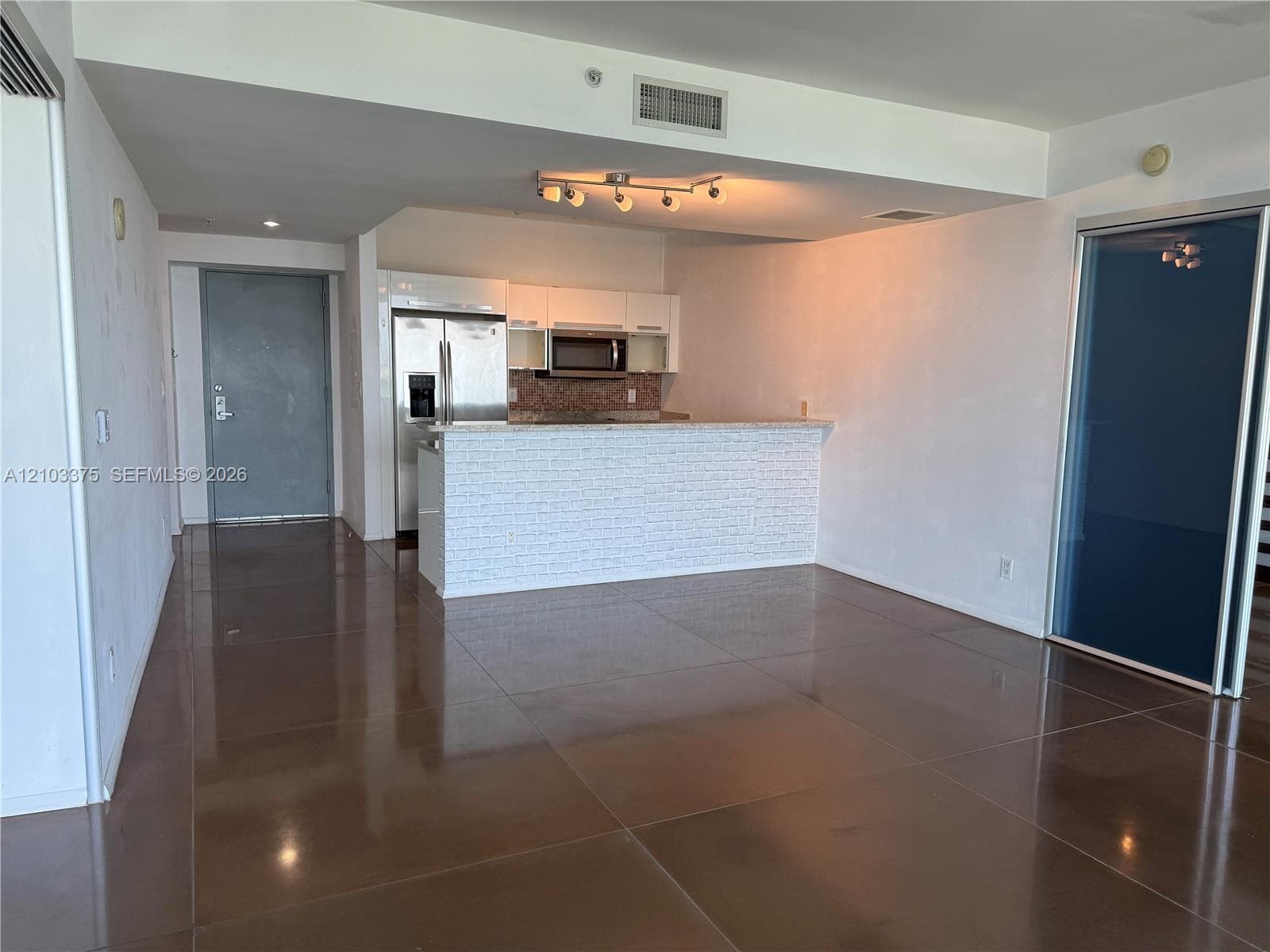 Kitchen featuring a breakfast bar with textured stone-style cladding, high-gloss white cabinetry, stainless steel appliances, and large-format tile flooring
