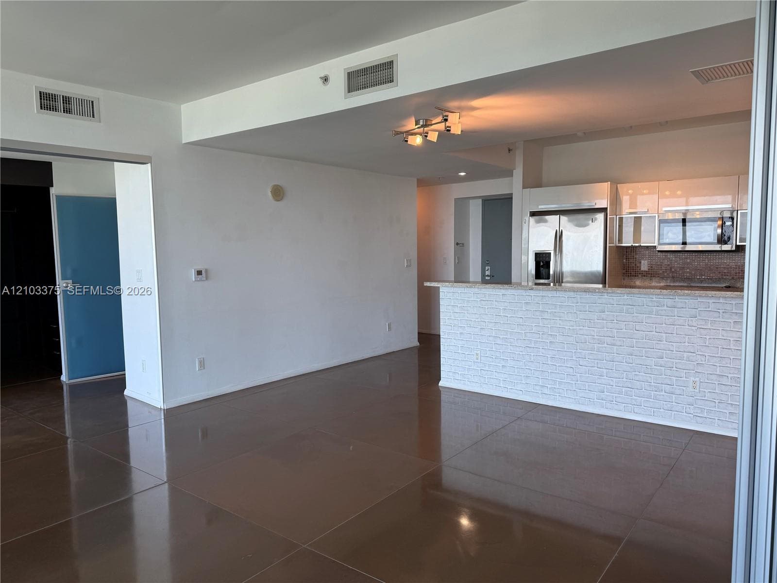 Open concept living area featuring large-format tile flooring, a kitchen breakfast bar with brick-style siding, stainless steel appliances, and multi-bulb track lighting