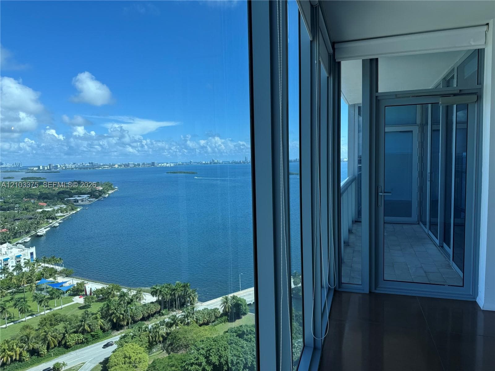 Floor-to-ceiling glass walls, expansive balcony with stone tile flooring, and metal-framed exterior door
