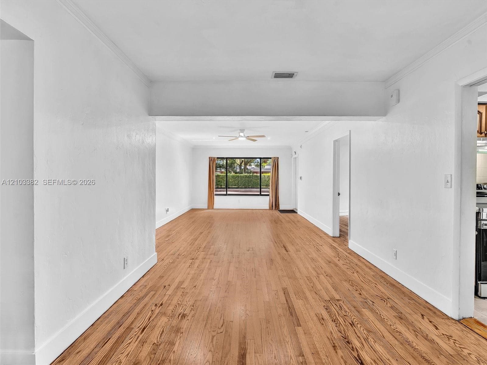 Open-concept split interior featuring wood-finish flooring, crisp white wall finishes, crown molding, ceiling fans. House for rent in Coral Gables. House for rent listed by Realtor.