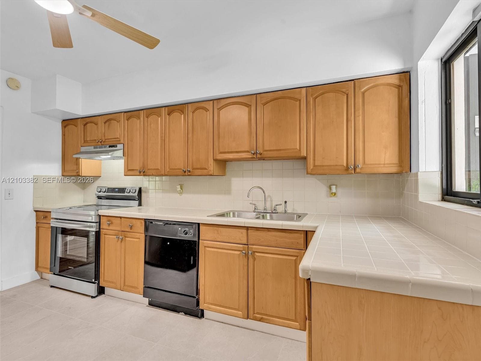 Kitchen featuring tile countertops, tile backsplash, stainless steel range, and integrated ceiling fan. House for rent in Coral Gables. House for rent listed by Realtor.