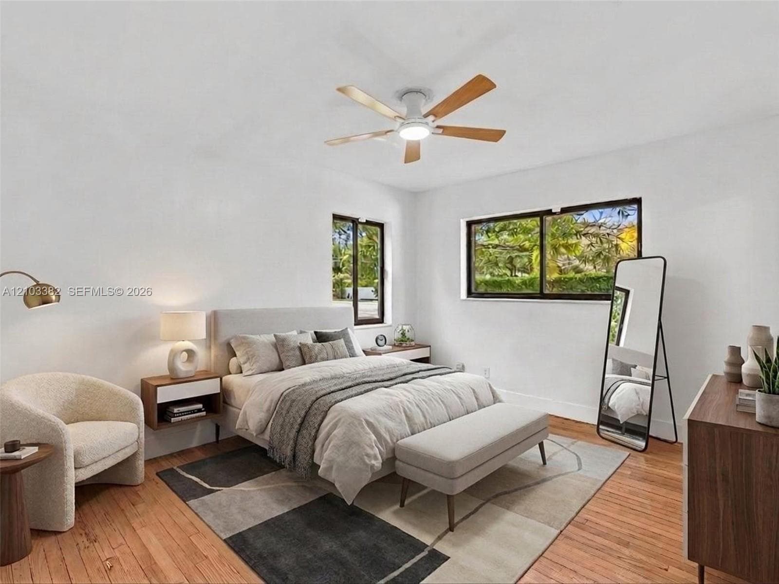 VIRTUAL STAGING. Front west bedroom with en-suite bath and closet. Featuring wood-finish flooring, two sliding windows with dark frames, and a ceiling-mounted fan with integrated lighting. House for rent in Coral Gables. House for rent listed by Realtor.