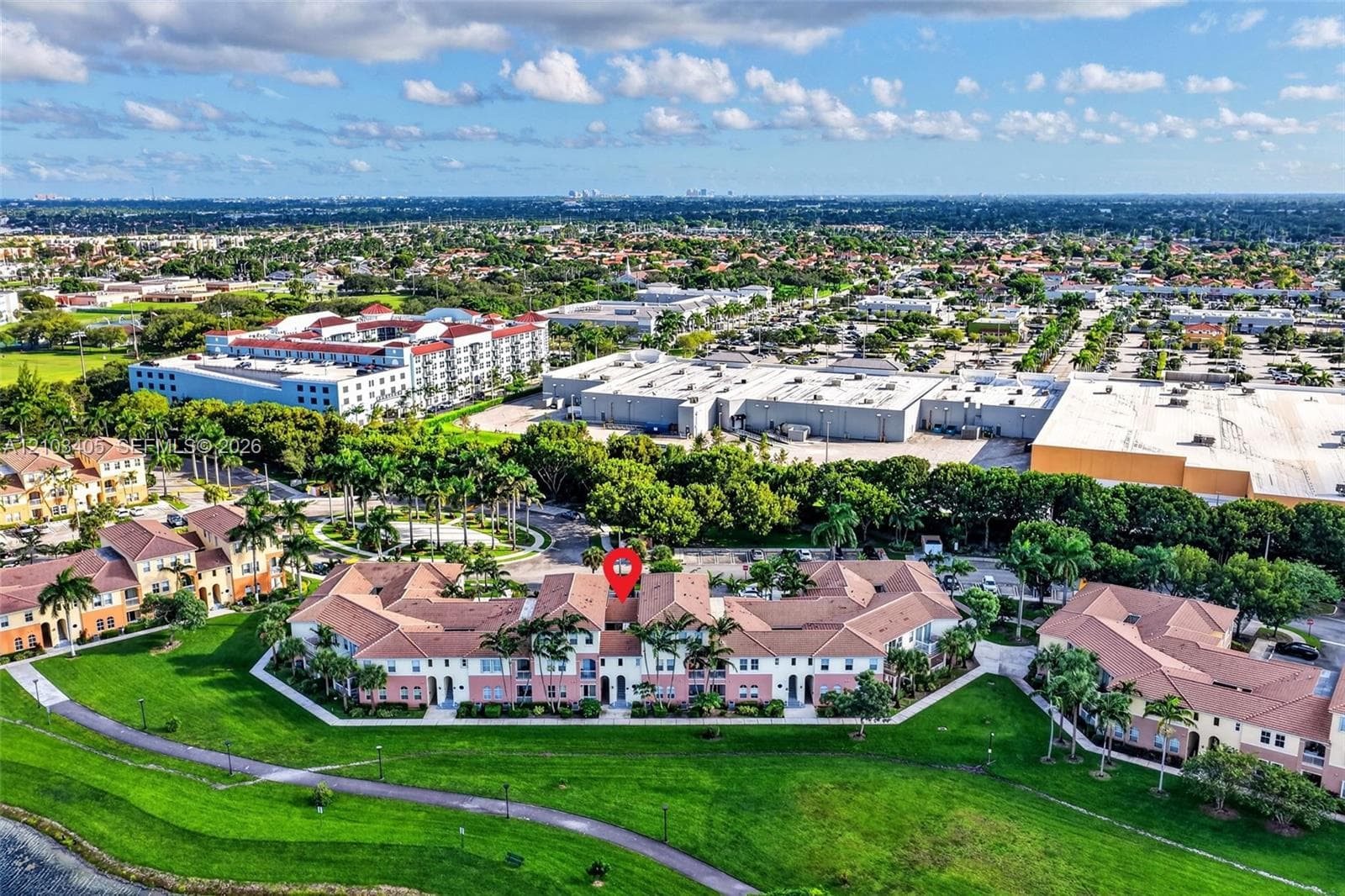 Aerial perspective featuring multi-story residential buildings with tile roofs, expansive green space, a paved walking path, and an encompassing waterfront