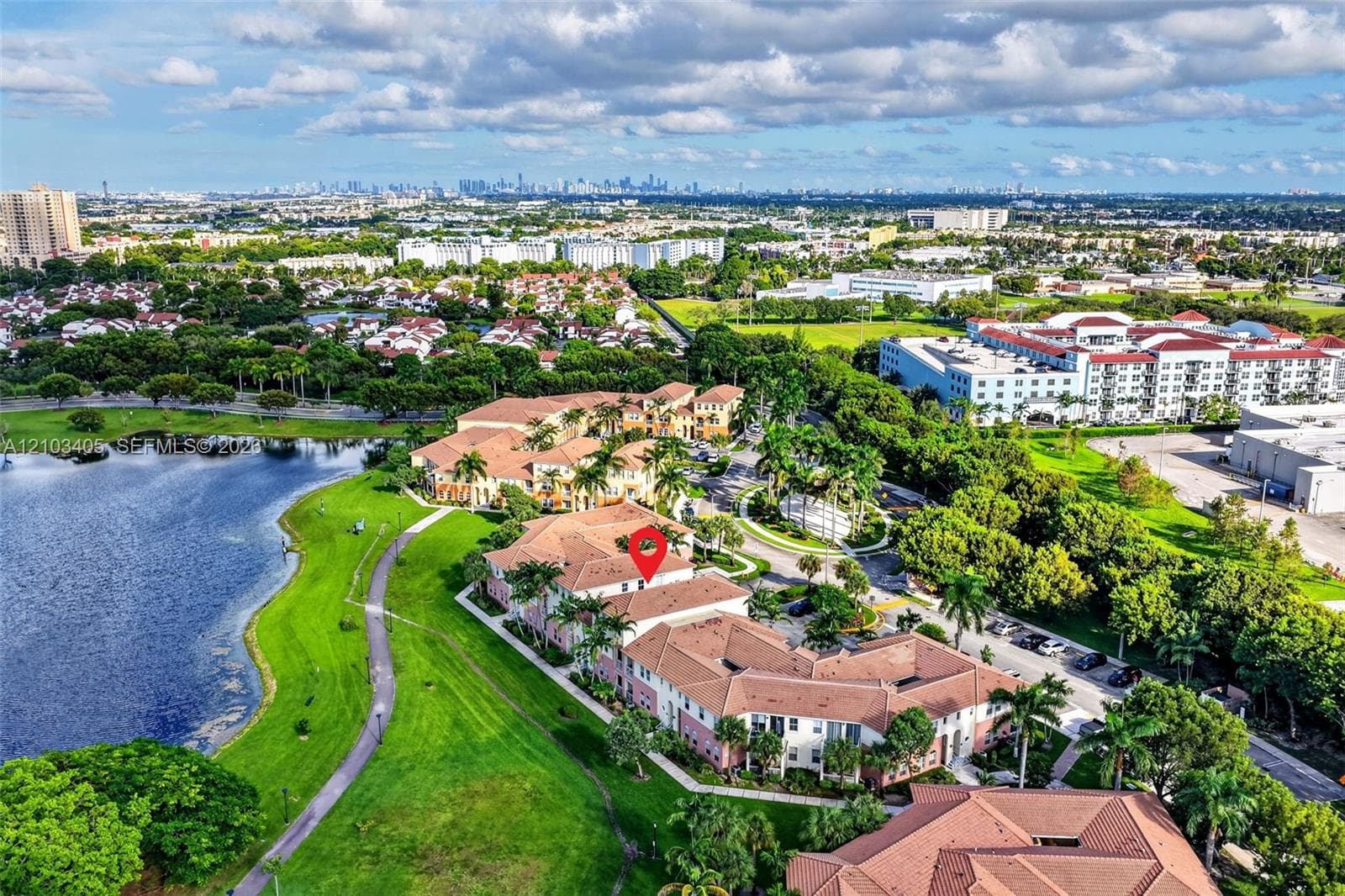 Aerial view of a multi-unit complex featuring clay-tile roofing, stucco exterior, paved parking areas, and mature palm tree landscaping