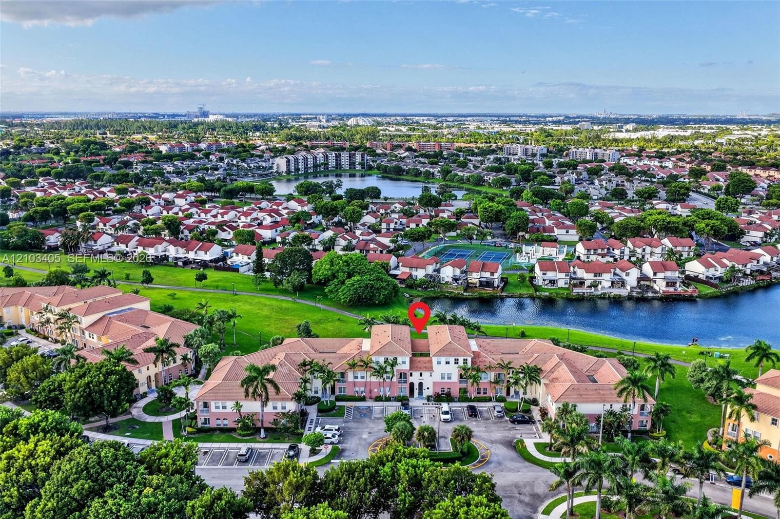 Aerial perspective of multi-unit residential complex featuring terracotta tile roofing, stucco exterior, surface parking, and extensive waterfront landscaping