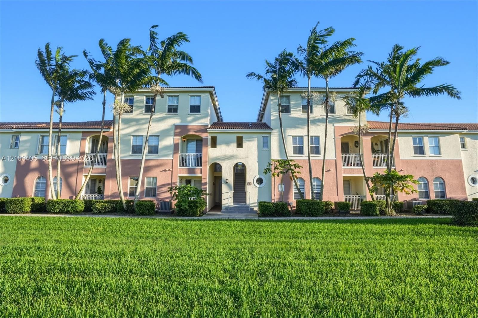 Multi-story stucco exterior featuring arched entryways, private balconies, clay tile roofing, and mature palm landscaping