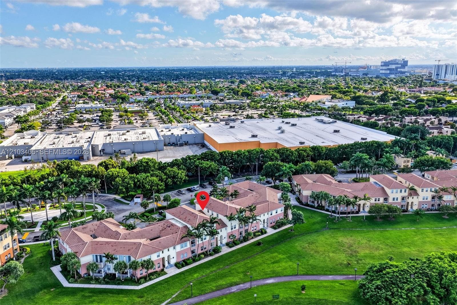 Aerial perspective featuring a multi-story building with a clay tile roof, situated near a lake, green space, and palm trees