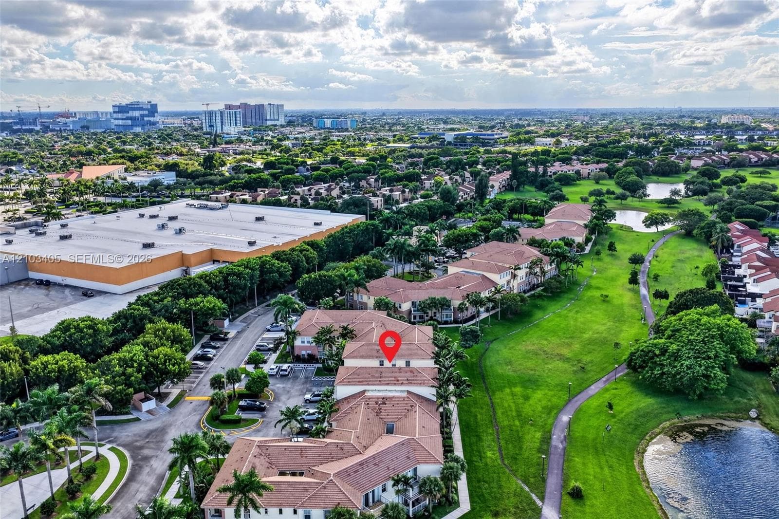 Aerial perspective featuring a multi-building residential community with red tile roofing, situated along a central lakefront with surrounding green space and mature landscaping