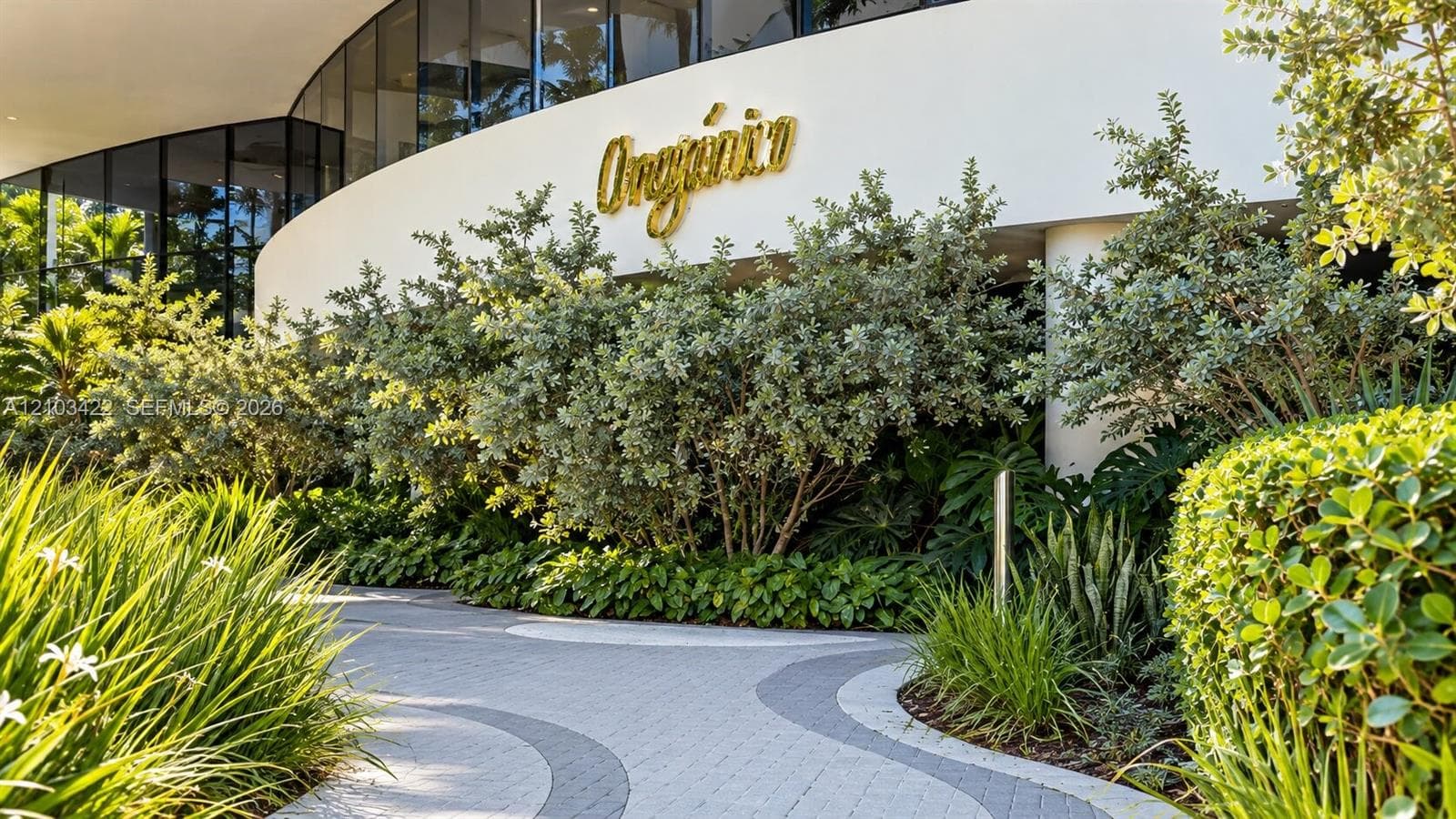 Landscaped entrance featuring a curving paver pathway, lush plantings, and a contemporary building facade