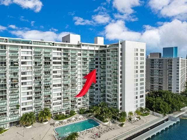 High-rise residential building featuring expansive private balconies with glass railings, a waterfront swimming pool, and paved terrace area