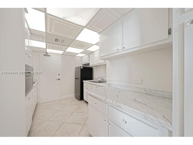 Kitchen featuring stone-patterned countertops, white cabinetry, integrated wall oven, tile flooring, and a luminous drop-ceiling panel system