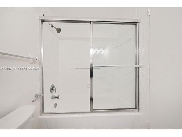 Bathtub and shower combination featuring a chrome sliding glass enclosure, white tile surround, and polished chrome fixtures