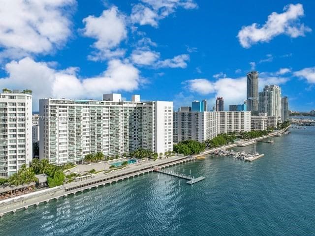 Waterfront high-rise building featuring private boat slips, an outdoor swimming pool, paved bulkhead, and perimeter landscaping