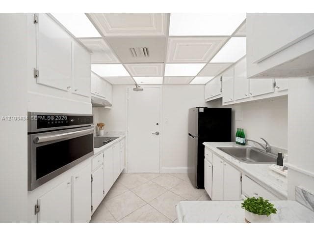 Kitchen featuring white cabinetry, stone-finish countertops, stainless steel wall-mounted oven, drop-in sink with metal faucet, and coffered ceiling panel lighting