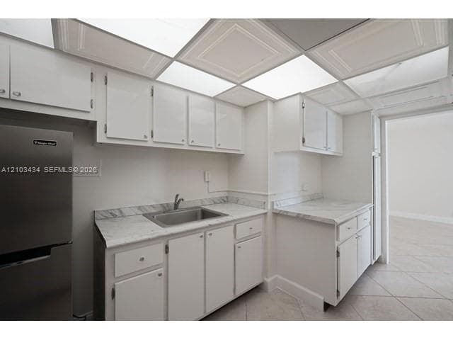 Kitchen featuring white cabinetry, stone-patterned laminate countertops, stainless steel sink, tile flooring, and drop-ceiling panels