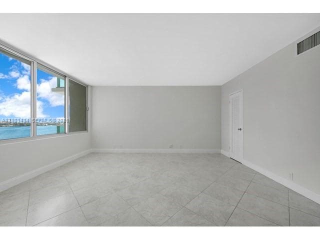 Floor-to-ceiling windows, neutral tile flooring, and water backdrop