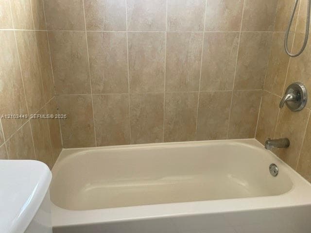 Bathtub featuring a neutral-toned tile surround and a chrome faucet set with a wall-mounted showerhead
