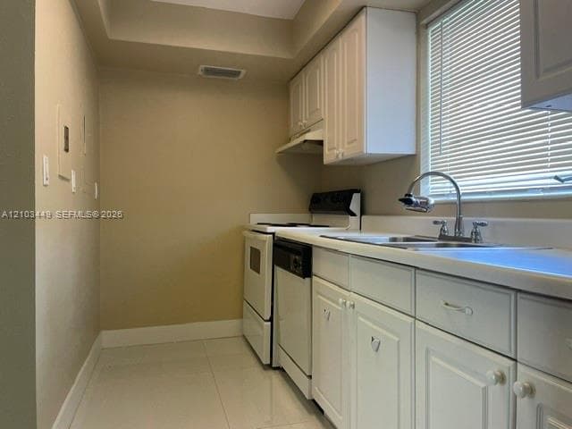 Kitchen featuring white shaker-style cabinetry, a dual-basin stainless steel sink with a high-arch faucet, white appliances, and light-toned tile flooring