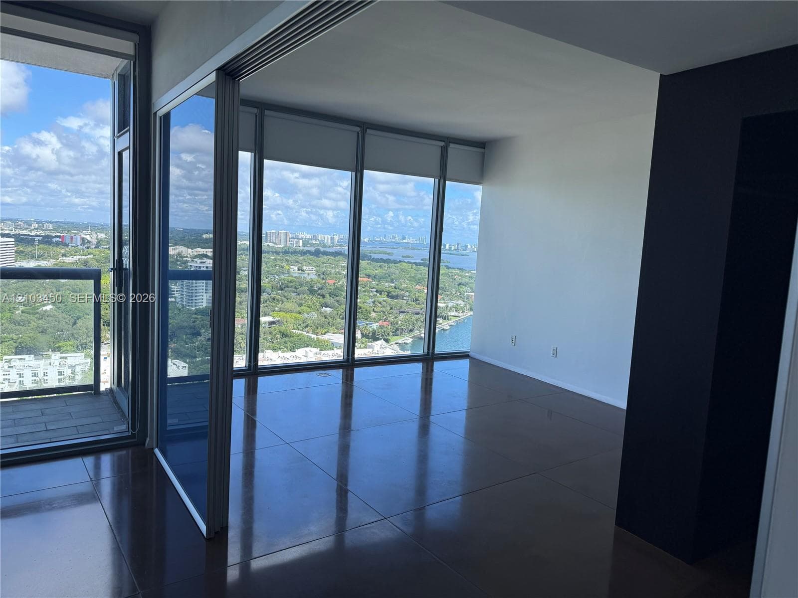 Floor-to-ceiling glass walls, large-format tile flooring, private balcony with metal railing, and high-rise exposure