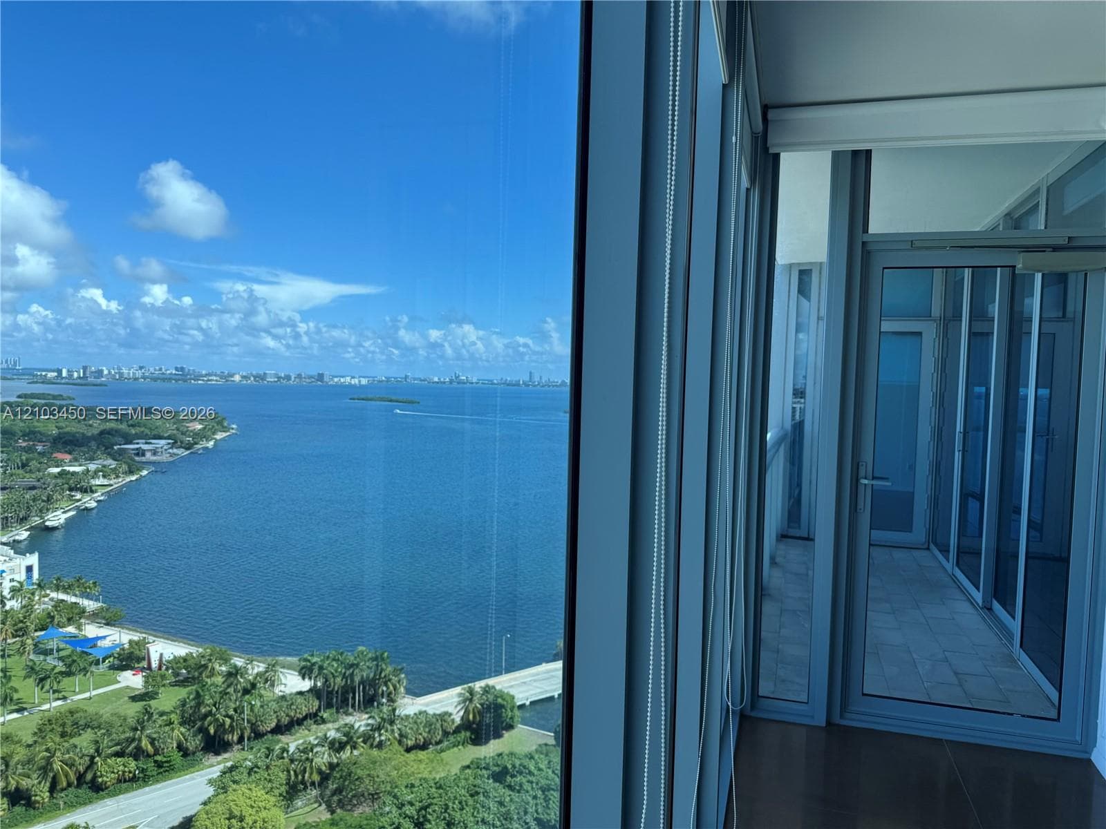 Floor-to-ceiling glass paneling, tile-floored balcony, and metal-framed door system with expansive water scenery