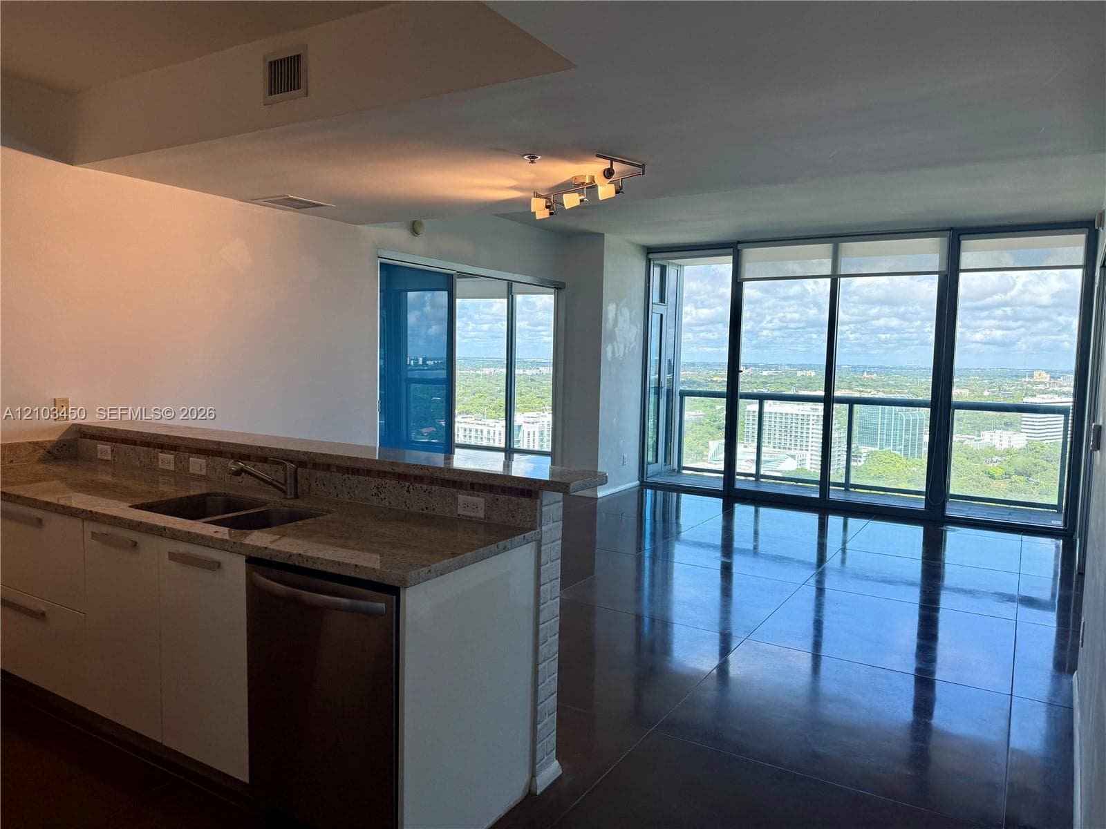 Kitchen featuring a stone-surface countertop, dual-basin under-mount sink, white cabinetry, and stainless steel dishwasher, complemented by floor-to-ceiling windows and high-gloss tile flooring
