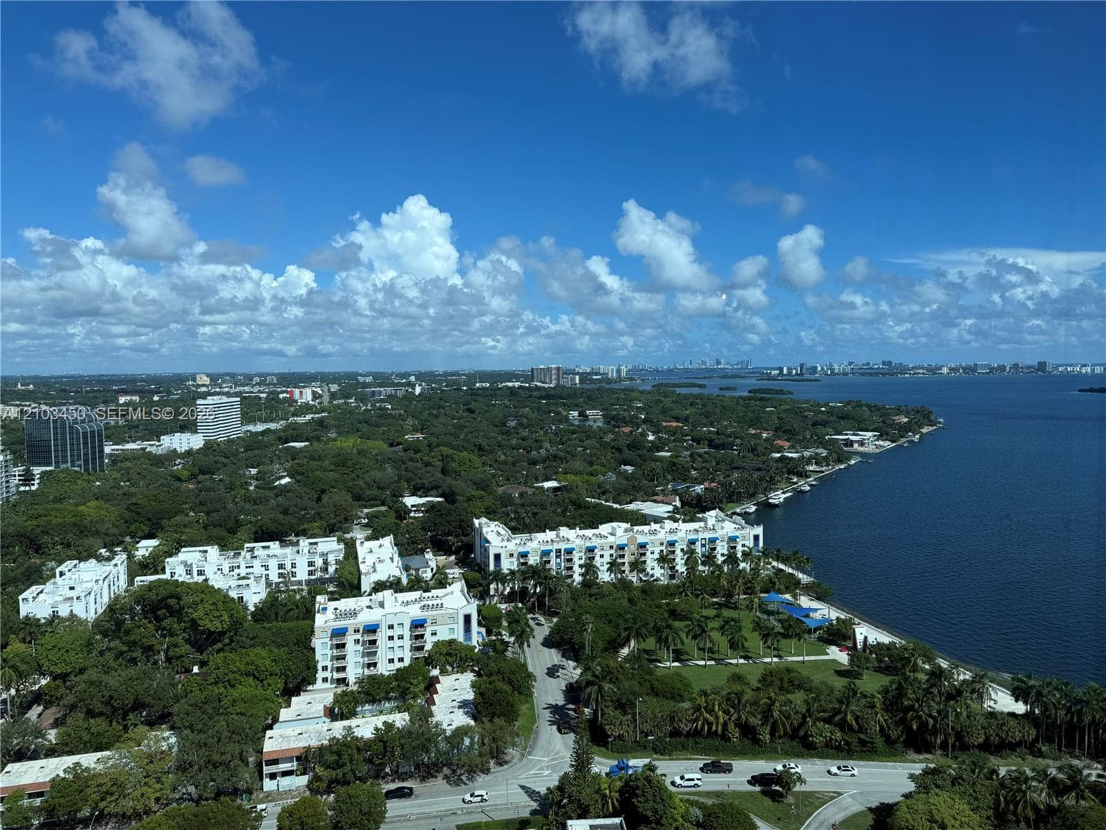 Aerial perspective featuring coastal shoreline, deep water access, expansive tree canopy, and metropolitan skyline